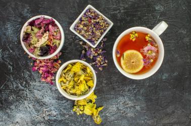 close up photo of herbal tea near bowls of dry flowers on grey background close up photo of herbal tea near bowls of dry flowers on grey background